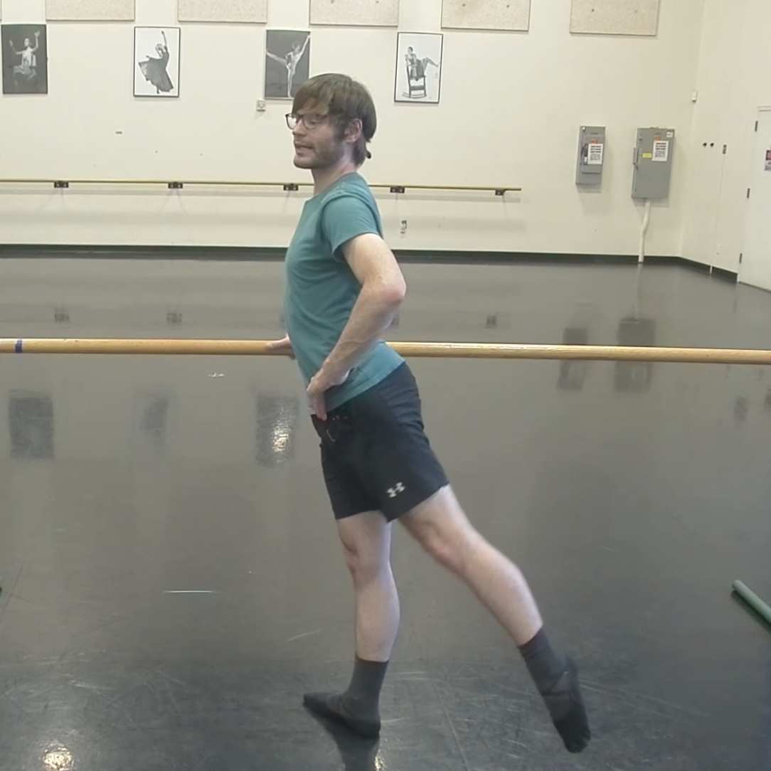 Christian stands at the barre with leg extended