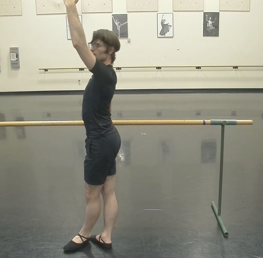 Christian stands at the barre with a hand over his head